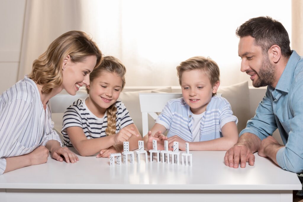 smiling family sitting at table and playing with domino pieces